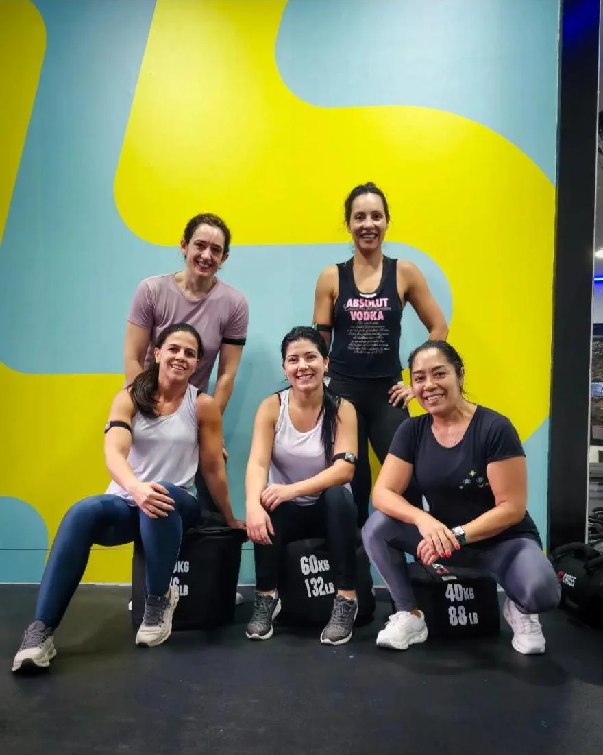 Cinco alunas posando agachadas e em pé com sacos de areia, na parede amarela do estúdio